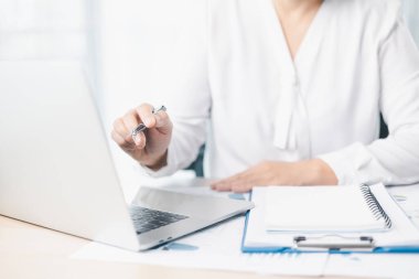 İş kadını elinde kalem tutarken ve hesap makinesiyle ofis masasında mali belgeleri incelerken dizüstü bilgisayarda çalışıyor. Muhasebe, iş planlaması, mali analiz ve verimlilik kavramı.