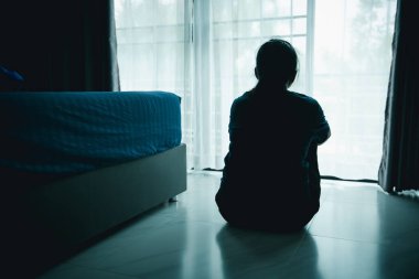 Yalnız bir kadın karanlık odada pencerenin yanında oturur ve dışarı bakar. Depresyon, endişe, üzüntü, yalnızlık, zihinsel sağlık sorunu, duygusal mücadele ve daha iyi bir yaşam umudu kavramı.