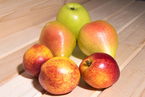 Red-yellow peaches, yellow pears, green apple lie on a wooden table close-up, fruit assorted
