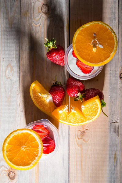 Sliced strawberries in half, orange sliced jars of yogurt on a wooden table