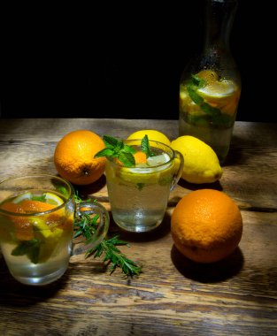 İki bardak ve bir şişe meyve, limon ve portakal, ahşap bir masada nane şekeri.