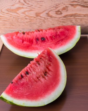 Olgun kırmızı bir karpuzun iki yarısı, ahşap bir masada, durgun bir hayat.