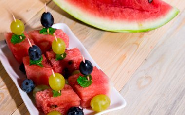 Parlak karpuz kanepeli bir tabak, bir dilim karpuz, üzümler, açık ahşap bir masada nane şekeri, natürmort.