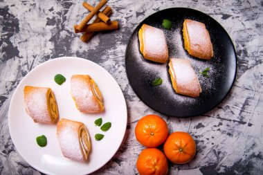 Strudel pişirme, mandalina yapraklı pudralı kek, tarçın çubukları beyaz, siyah ve beyaz arka planda siyah bir tabak, metin için bir boşluk, üst görünüm