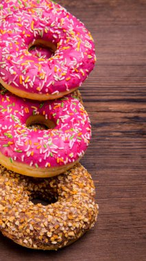Ahşap zemine serpiştirilmiş pembe çikolatalı donutlar, yazı için boşluk, yakın çekim -