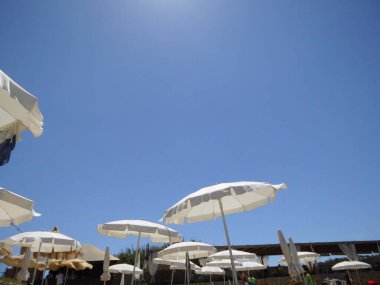 Mavi gökyüzüne karşı beyaz plaj şemsiyeleri. Marfa, Mellieha, Malta 