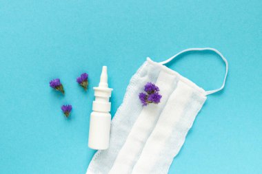 Mevsimlik bahar alerjisi çiçek konsepti. Beyaz sprey kutusu, mor çiçekli peçeteler ve mavi arka planda tıbbi koruyucu maske. Yaratıcı düz konum, kopyalama alanı, asgari biçim