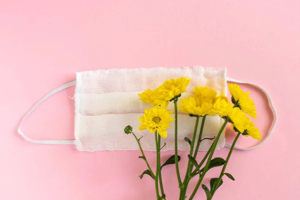 Seasonal spring summer allergy flowers concept. Yellow flowers with medical protective mask on pink background. Creative flat lay composition, copy space, minimal style