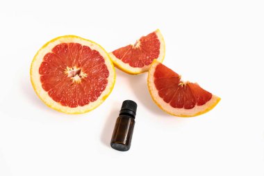 Olgun kırmızı bir bütün ve beyaz arka planda bir şişe aroma yağıyla dilimlenmiş greyfurt. Minimum meyve konsepti, güzellik teması ve aromaterapi.