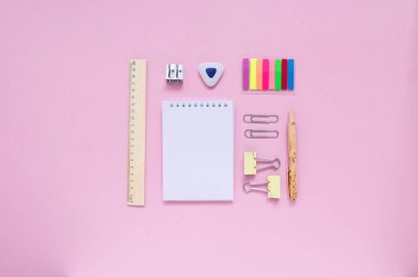 Sabit, okula dönüş, yaratıcılık ve eğitim konsepti. Not defteri, kalem, silgi, cetvel, ataç, zımba ve pembe arka planda fırça, düz yatak. Üst görünüm