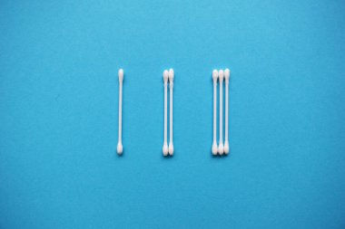 Mavi arka planda pamuk tomurcukları ve süngerlerden sayılar. Plastik pamuklu bez. Üst Manzara. Kozmetikleri kaldırmak için düz konum bileşimi ürünleri.