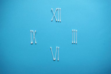 Mavi arka planda pamuk tomurcukları ve süngerlerden yapılmış yaratıcı saatler. Plastik pamuklu bez. Üst Manzara. Kozmetikleri kaldırmak için düz konum bileşimi ürünleri.