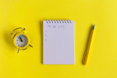 Yazılı not: listelenecek, sarı zemin üzerinde saat ve kalem, masanın üzerinde spiral defter. İş, eğitim eğitimi. Monokrom sarısı ve minimalizm. Düz üst görünüm.