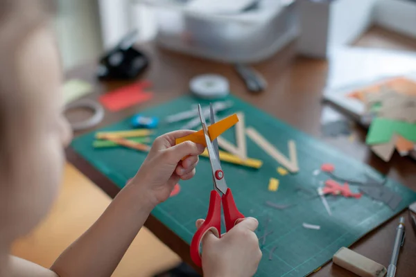 Uma menina de sete anos corta com uma tesoura de papel amarelo . — Fotografia de Stock