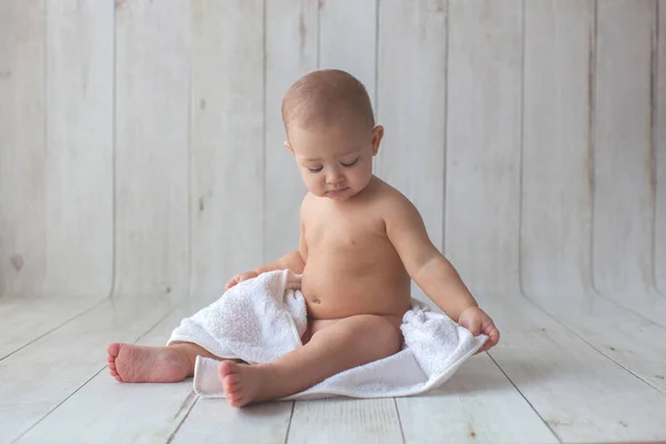 Little baby sitting in a white towel on wooden background. — Stockfoto