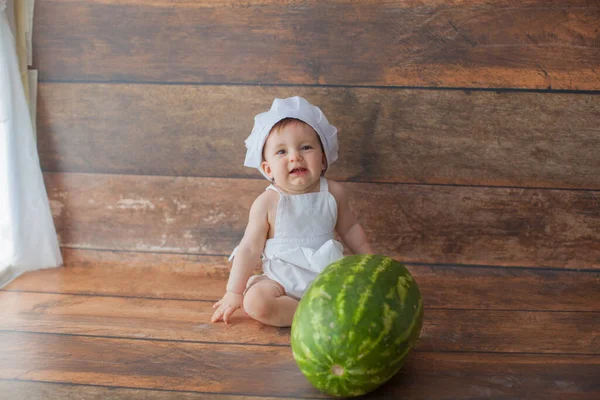 Bir yaşında bir kız elinde karpuzla oturuyor. Şef kostümü giymişti..