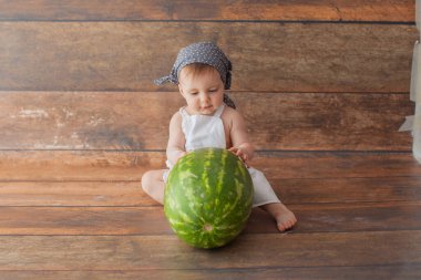 Bir yaşında bir kız elinde karpuzla oturuyor. Şef kostümü giymişti..