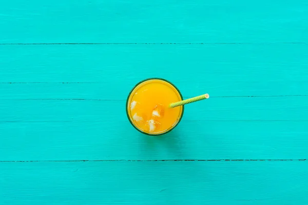 Orange juice in a glass on turquoise blue wooden table, top view, flat lay