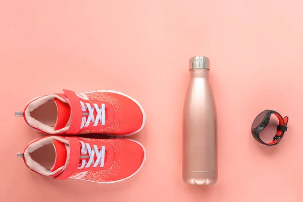 Red sneakers, sport watch and bottle with water on coral pink background. Concept of healthy life, sport and training, top view, copy space.