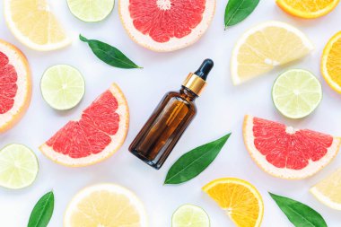 Kozmetik serumlu cam şişe ve beyaz arka planda dilimlenmiş narenciye meyvesi.