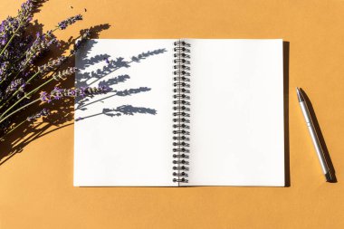 Lavanta çiçekleri ve kalemle bej arka planda boş not defteri. Üst görünüm, düz görünüm, kopyalama alanı.