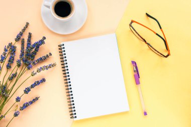 Sarı arka planda, lavanta çiçekleri, kahve fincanı, kalem ve bardaklarla boş bir not defteri oluşturun. Üst manzara, düz uzanma