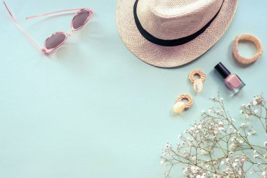 Mavi arka planda kadın aksesuarlarıyla yatıyordu. Güneş gözlüğü, hasır şapka, küpeler, bilezik ve çigila çiçekleri..