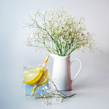 Bir bardak samanlı limonata ve beyaz sürahide çigila çiçeği.