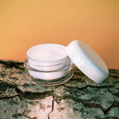 Ağaç kabuğunda beyaz kavanozda yüz kremi, turuncu arka plan. Doğal kozmetik konsepti