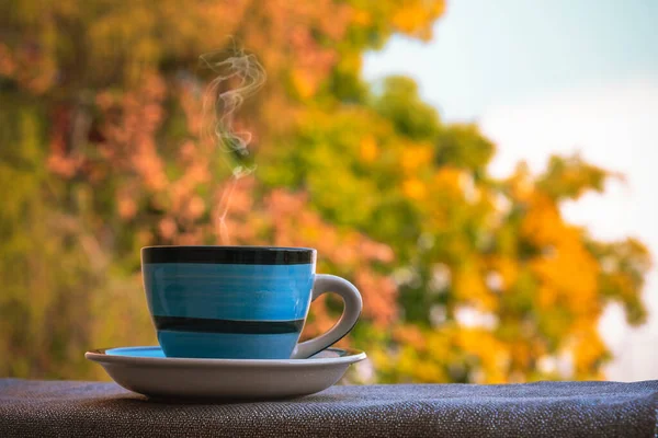 Blue cup with hot drink on yellow autumn foliage background — Stock Photo, Image