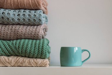 Bir yığın sıcak örülmüş kadın kazağı ve beyaz arka planda bir fincan sıcak içecek. Sonbahar ya da kış konsepti