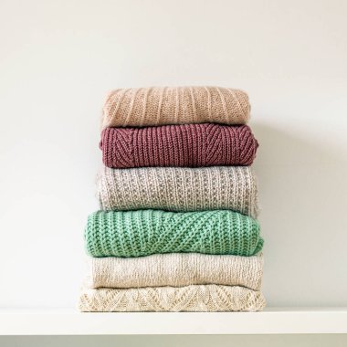 Beyaz arka planda sıcak örülmüş kadın kazağı yığını. Sonbahar ya da kış konforu.