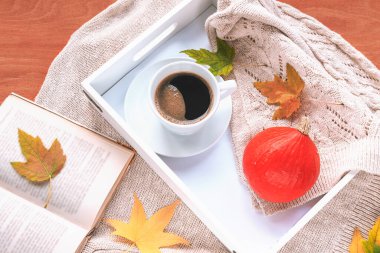 Tepside bir fincan kahve, balkabağı, sonbahar yaprakları, bir kitap ve örülmüş bir kazak. Sonbahar konsepti, üst görünüm.