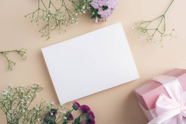 Çiçekli bir hediye kutusu ve bej arka planda boş bir kart. Üst görünüm, düz görünüm, model.