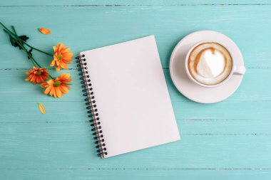 İçinde kahve fincanı ve turkuaz ahşap arka planda çiçekler olan sarmal defter. Üst görünüm, düz görünüm, model.