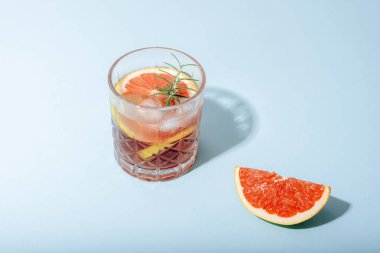 Meyve dilimli greyfurt kokteyli ve mavi arka planda keskin gölgeli biberiye. Yakın çekim..