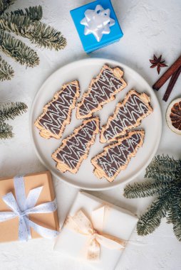 Çikolata kaplı Noel ağacı kurabiyelerinin en üst görüntüsü, şenlikli dekorasyonlar, köknar dalları ve beyaz arka planda hediyeler. Üst manzara, düz uzanma.