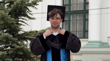 Proud graduate with a cap on his head arranges his graduation gown to go to solemnly receive his international diploma of higher education graduation from the university. Higher education concept