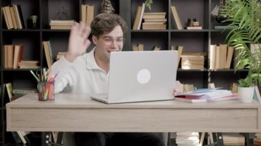 Handsome young boy waving in front of a computer while participating in an international workshop online. Student with glasses connected to online distance learning lessons