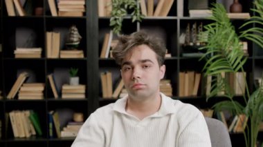 Freelancer boy leans back on chair and takes a break from work. Tired and exhausted young man has eye and back pain from working long hours from home remotely with laptop. Remote job