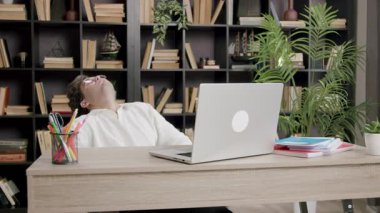 Disappointed boy leans back on chair at office table. Young man disappointed and angry because he fails a project for college. Student preparing for university on computer