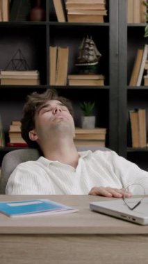 Öğrenci çalışmaya ara verir ve gözlerini ve ellerini dinlendirir. Modern bir kütüphanede yorgun bir çocuk ekstra çalışır ve bir dizüstü bilgisayarın önünde derslere hazırlanır ve notlar alır.