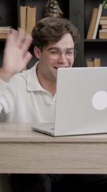 Handsome young boy waving in front of a computer while participating in an international workshop online. Student with glasses connected to online distance learning lessons
