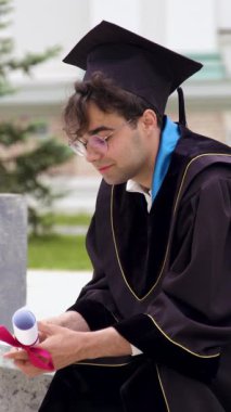 Mezuniyet elbiseli, siyah cüppeli ve şapkalı üniversite kampüsünün avlusunda bir sandalyeye oturmuş mezuniyet diplomasını gururla elinde tutuyordu. Uluslararası Çalışmalar