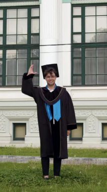 Siyah bornoz giymiş genç bir öğrenci mutlu ve coşkulu bir şekilde zıplayıp elbisesini kaldırıyor. Lisansüstü öğrencisi yüksek eğitimli bir diploma almayı başardığı için mutlu. Başarılarının tadını çıkarıyor.