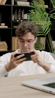 Okulun kampüs kütüphanesinde akıllı telefondan online spor videoları izleyen şaşkın, heyecanlı çocuk. Üniversite bankında elinde telefonla çevrimiçi mobil oyunlarda erkek kazanan