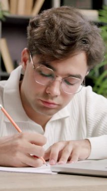 Genç uzman online ileri eğitim dersleri alıyor, dizüstü bilgisayardaki hoparlörleri dinliyor ve not defterine not alıyor. Çocuk, çevrimiçi kurslar ve konferanslar sayesinde kariyerinde büyüyor.