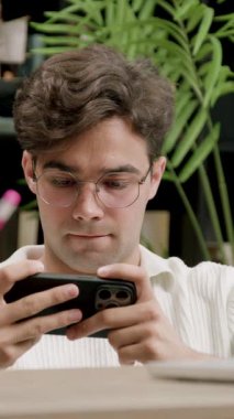 Okulun kampüs kütüphanesinde akıllı telefondan online spor videoları izleyen şaşkın, heyecanlı çocuk. Üniversite bankında elinde telefonla çevrimiçi mobil oyunlarda erkek kazanan