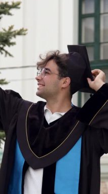 Modern graduate boy with cap on his head and graduation gown poses and takes selfies on his phone to send to his parents and friends. Pictures from the graduation ceremony for graduating students