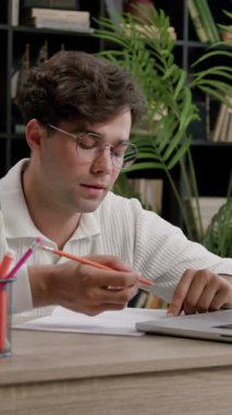 Öğrenci çocuk modern bir kütüphanede okuyor. Gözlüklü genç adam ofis masasında oturmuş internette bilgi arıyor ve not defterine not alıyor.